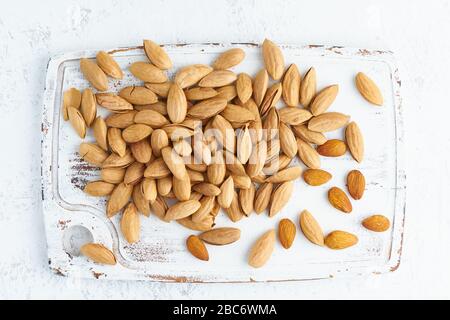 Top view almonds in endocarp, bowl with drupe in shell on white wooden cutting board Stock Photo