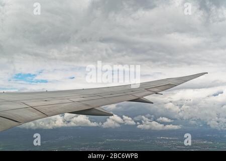 Airplane wing against clouds and earth. View from airplane porthole while flying Stock Photo