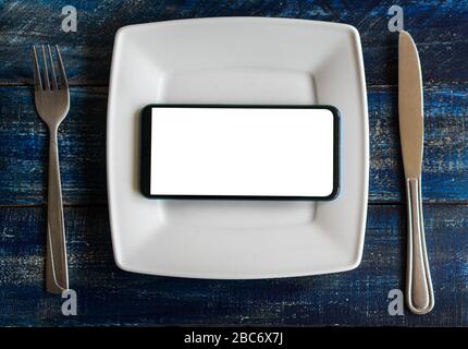 Mobile smart phone served as dinner on white plate. Concept of information absorption process, Internet addiction. Dependence on the phone, smartphone Stock Photo