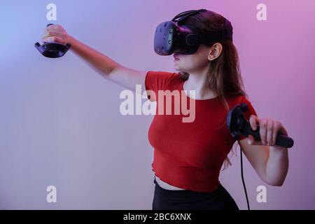 A brown-haired woman in a red jacket plays virtual reality. The room is filled with neon colors. High quality photo Stock Photo