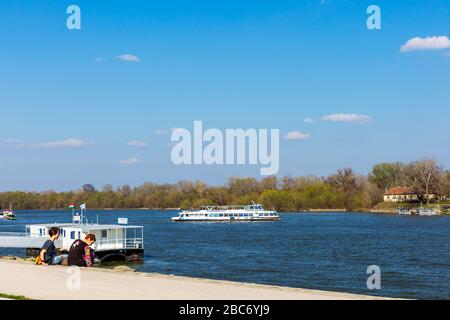 Szentendre, Hungary - April 08, 2018: Tourist boat on Szentendre branch of Danube River on sunny day. Family resting on the shore. Space for text Stock Photo