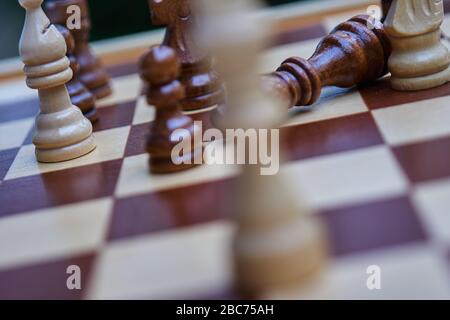 Intentionally crooked chessboard with blurred white king and toppled black king in the background, concept Stock Photo