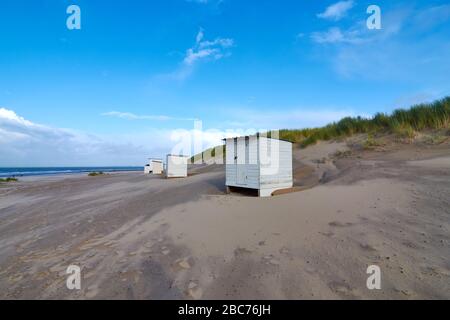 Small white locker house at the North Sea beach in the Netherlands. The blue sky is interspersed with clouds.