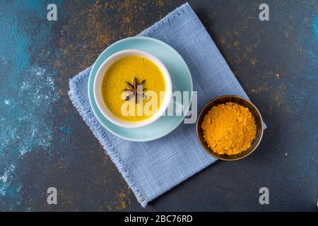 Flay lay Ayurvedic golden turmeric latte milk tea made with turmeric and other spices on blue background. Healthy medicine drink. Stock Photo