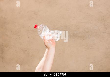 Hand holding smashed empty plastic bottle isolated on a blurred background. Recycle and volunteer concept. Environmental pollution and worldwide ecolo Stock Photo
