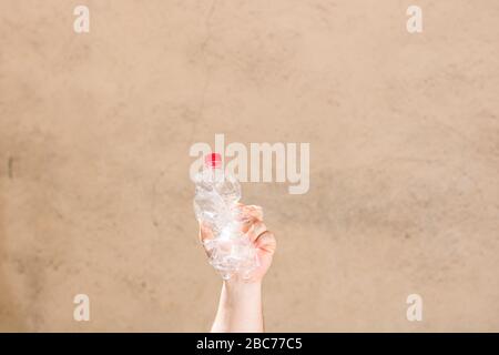Hand holding smashed empty plastic bottle isolated on a blurred background. Recycle and volunteer concept. Environmental pollution and worldwide ecolo Stock Photo