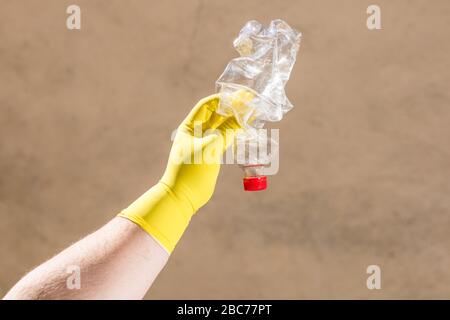 Hand with rubber glove holding smashed empty plastic bottle isolated on a blurred background. Recycle and volunteer concept. Environmental pollution a Stock Photo