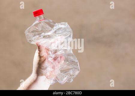 Hand holding smashed empty plastic bottle isolated on a blurred background. Recycle and volunteer concept. Environmental pollution and worldwide ecolo Stock Photo