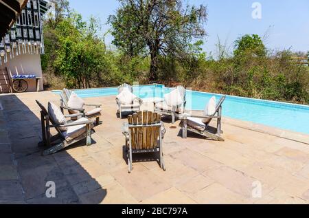 View of the outdoor blue swimming pool and wooden poolside chairs on a sunny day, Denwa Backwater Escape, Satpura, Madhya Pradesh, central India Stock Photo