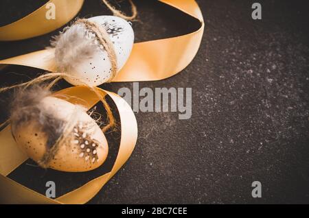 Easter background with decorations. Decorative easter eggs with feathers and ribbon on a dark concrete background. Stock Photo
