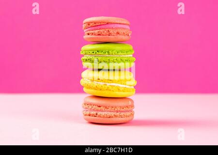 Multi-colored macaroons stand in a pile on a pink table Stock Photo