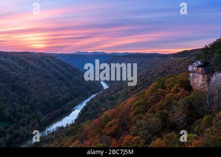 The low evening sun sets over Beauty Mountain in the New River Gorge of West Virginia, creating purple pastels in the sky above the autumn landscape a Stock Photo