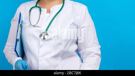 medic woman in white coat, blue latex gloves holding a tablet with a clip for papers, blue background, place for an inscription Stock Photo