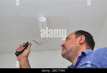 Man painting ceiling in white color with a roller Stock Photo