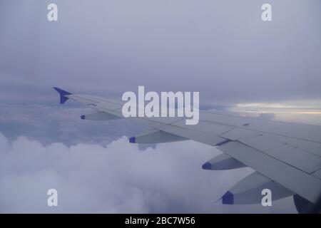 Wing of an airplane flying above the rainy dark clouds. Shot of Plane wings colored white and blue. Stock Photo