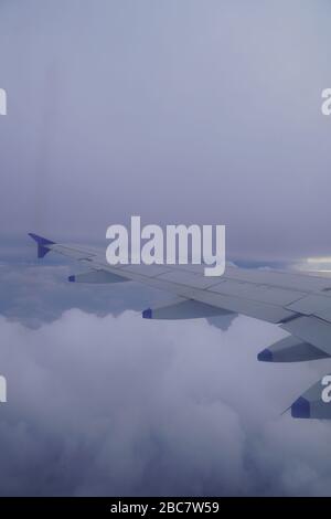 Wing of an airplane flying above the rainy dark clouds. Shot of Plane wings colored white and blue. Stock Photo