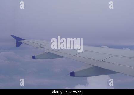 Wing of an airplane flying above the rainy dark clouds. Shot of Plane wings colored white and blue. Stock Photo