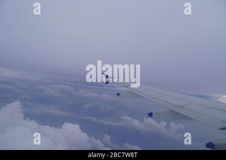 Wing of an airplane flying above the rainy dark clouds. Shot of Plane wings colored white and blue. Stock Photo