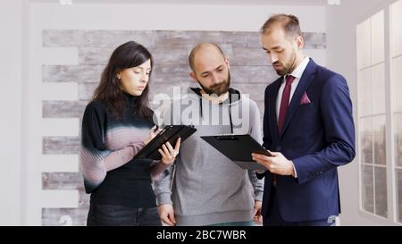 Real estate agent in business suit talking about finances with clients to buy new apartment. Broker with clients in empty apartment. Stock Photo