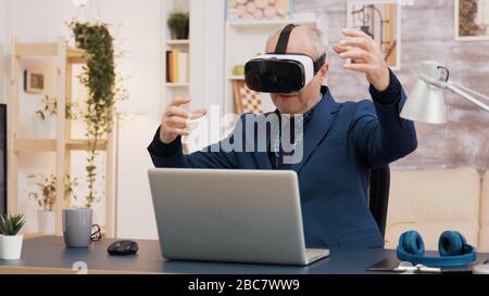 Retired man experiencing virtual reality using vr headset in living room. Cup of coffee on the table. Stock Photo