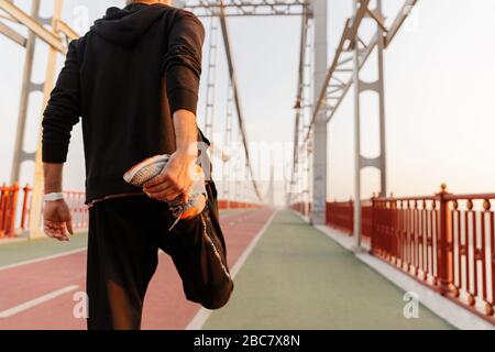 Back view of a young fit sportsman working out on a bridge, doing stretching exercises Stock Photo