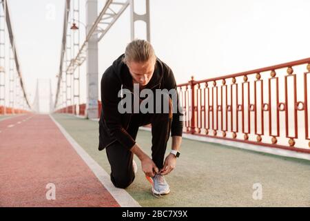 Attractive young fit sportsman working out on a bridge, tying shoelace Stock Photo