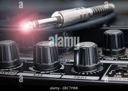 close up of a jack plug for electric guitar resting on the panel of an amplifier with detail of the valves for the various adjustments and light effec Stock Photo