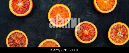 Blood Oranges. Halved blood oranges scattered on a black stone background. Banner. Stock Photo