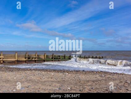 Waves crashing against a costal defence groin on a sunny day with blue skys. Stock Photo