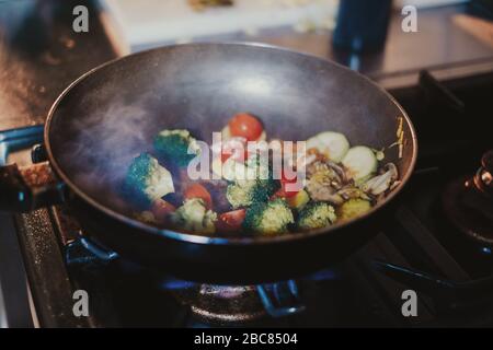 Various vegetables cooking in frying pan on the stove and steam comming out Stock Photo