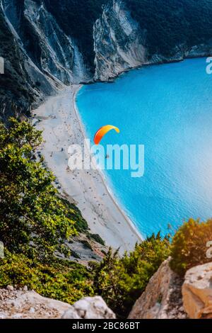 Figure of a parachutist skydiver with orange parachute against a blue lagoon of Myrtos Beach, Kefalonia Island, Greece. Stock Photo