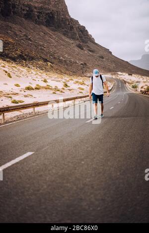 Traveler with backpack standing in the center of an epic winding road. Huge volcanic mountains in the distance behind him. Sao Vicente Cape Verde. Stock Photo