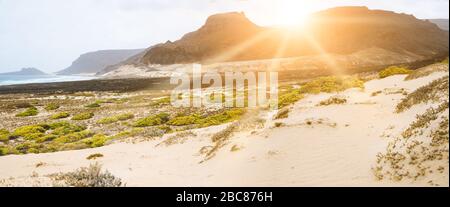 Amazing sunset over volcanic mountains on desolated atlantic coast. Sunrays falling on coastal dunes Sao Vicente Cape Verde. Stock Photo