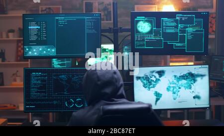 Back view of hooded cyber terrorist using super computer in dark room. Team of hackers. Stock Photo