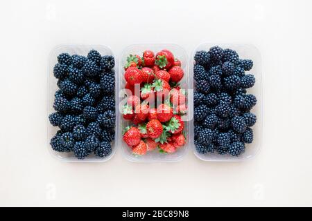 Three plastic containers full of fresh blackberries and strawberries, top view. Stock Photo