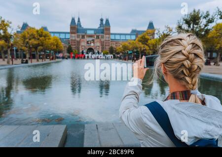 Woman tourist taking photo of the Rijksmuseum in Amsterdam on the mobile phone. Travel in Europe city trip concept. Stock Photo