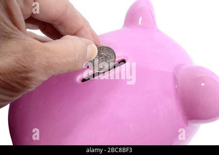 Horizontal close-up shot of a woman’s hand about to drop a quarter into the slot of a pink piggy bank.  White background. Stock Photo