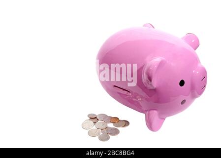 Horizontal shot of a pink piggy bank lying on its side with the slot on top facing toward the camera.  Pile of coins next to it.  White background.  C Stock Photo