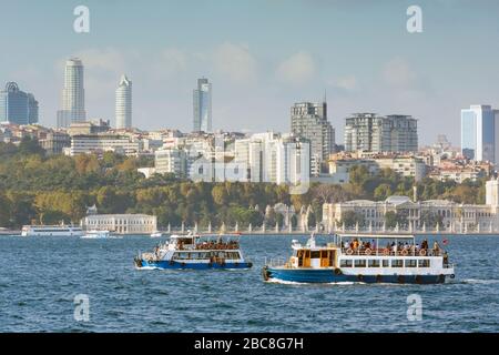 Istanbul, Turkey.  Ferries on the Bosphorus. Dolmabahce Palace on shoreline right. Modern buildings behind. Stock Photo