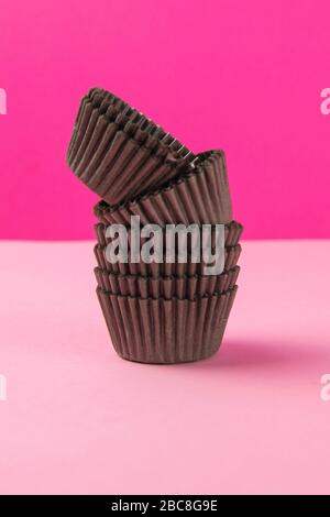 Pink background with brown paper forms for muffins. Close-up Stock Photo