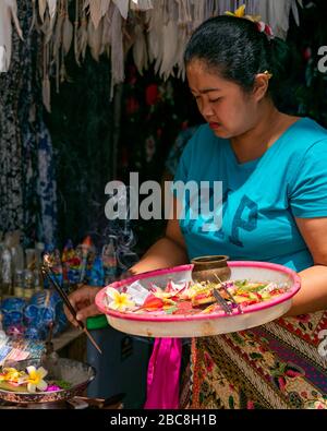 Vertical portrait of woman using flowers and incense to bless a new shop in Bali, Indonesia. Stock Photo