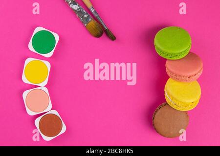Makarons on a pink background are next to the colors of macaroons and brushes for drawing Stock Photo