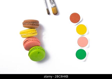 Makarons on a white background are next to the colors of macaroons and brushes for drawing. Top views with clear space Stock Photo