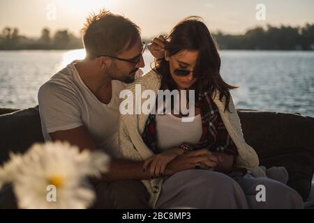 Troubled couple in love holding hands while sitting by the river. Beautiful autumn sunset Stock Photo