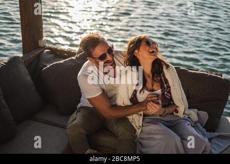 Couple laughing and  hugging while sitting by the river. Beautiful autumn day Stock Photo