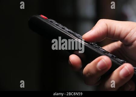 Hand holding remote control sitting on sofa . Stock Photo