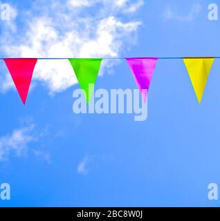 Bright colorful triangle flags on a string, blue sky with white fluffy clouds. Stock Photo