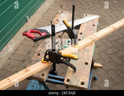DIY using Workzone Quick Ratcheting Bar Clamps to hold a wooden workpiece onto a B&D Workmate workbench while sawing. Stock Photo