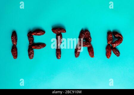 'Iftar' word made of delicious date fruits on blue background. Ramadan kareem with arabic dates. Stock Photo