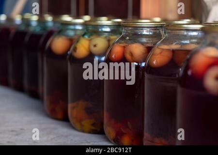 Natural home-made fruit drink. Compote of apples in glass jars sealed with metal lids. Drink storage. Blurred background. Side view. Stock Photo